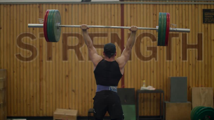 Man with black cap shirt and shorts lifts up heavy barbel