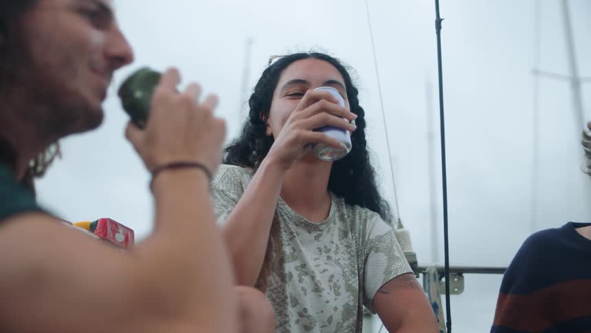 Young couple of happy friends toast with beer on a sailboat