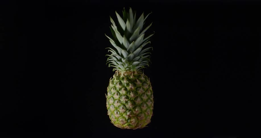 Fresh green and yellow pineapple spinning slowly in the air creating a contrast with black background