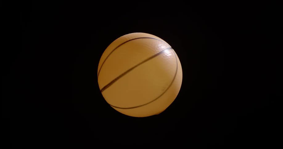 A rotating orange basketball suspended in the air while spinning in front of a black background