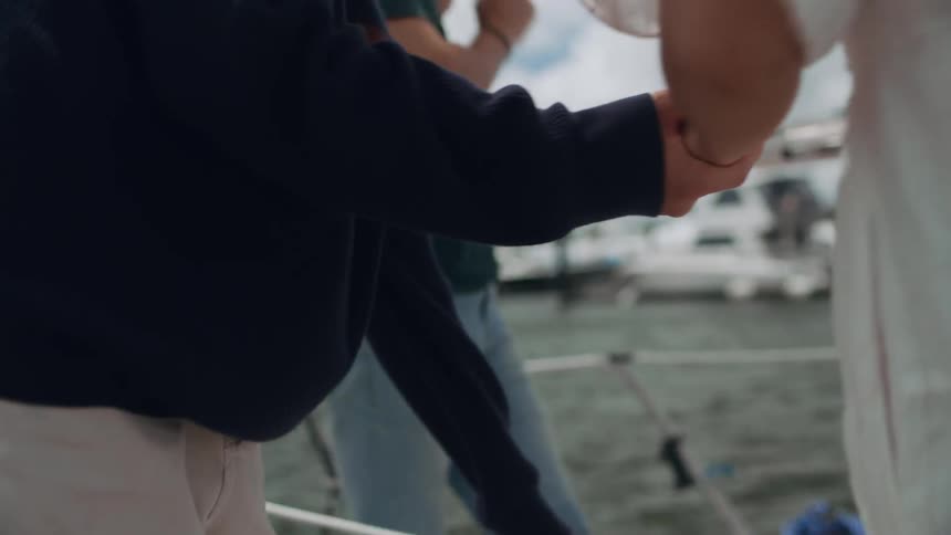A man helps a woman onto a boat docked on the coast