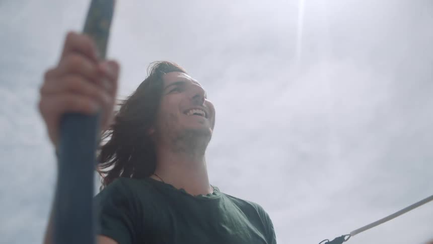 Young happy man with long hair waving in the wind on a sailboat at daytime