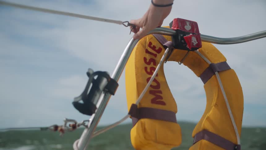 Close up of a yellow lifeguard hangin on a railing on the side of a sailing boat in the ocean