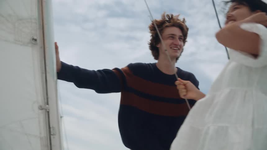 A young woman laughs as she tries to control her windblown hair while holding a line on a sailboat