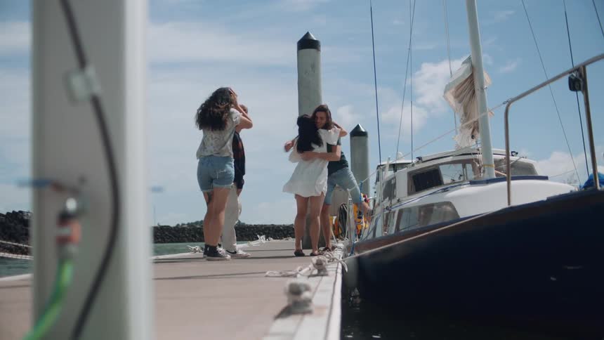 Friends greet each with hugs on dock near sailing boat