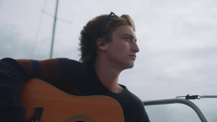 A male is sitting outdoors and holding a guitar