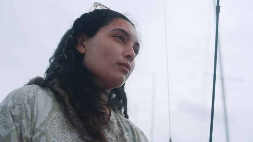 Woman with curly hair sunglasses and t shirt looks into space on boat on a cloudy day