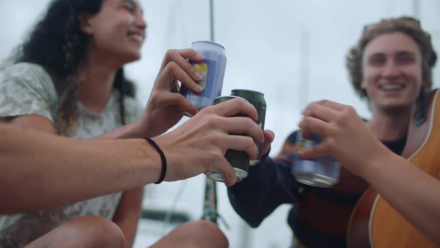 Group of happy friends sitting on a sailboat toast with soda or beer