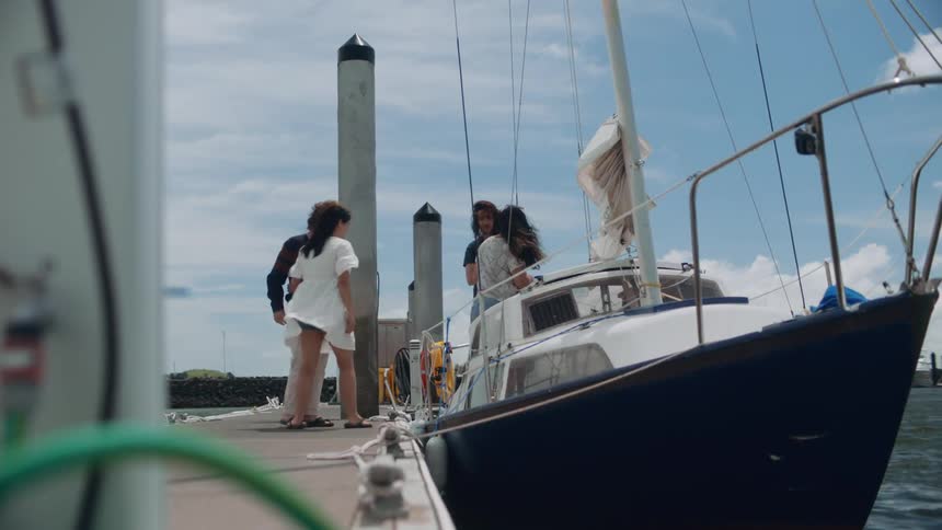 A small group of male and females greeting each other next to a boat and then getting on the boat