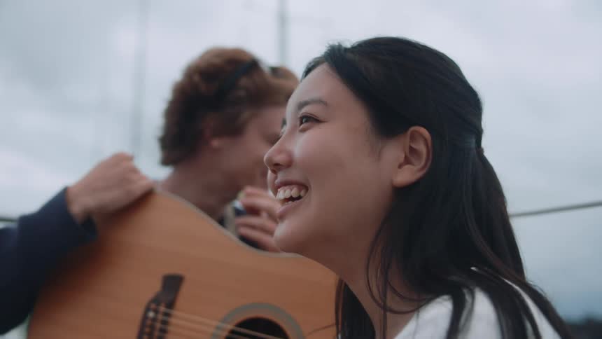 Man and woman laugh while sitting on sailboat with a guitar