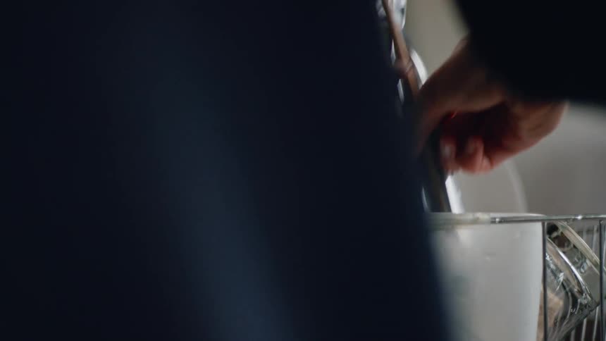 Close up of a person placing cutlery on a drying rack near the kitchen sink