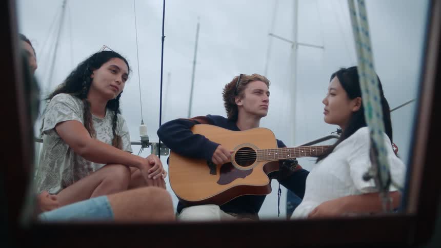 Young man plays guitar for his friends on a sailboat at daytime
