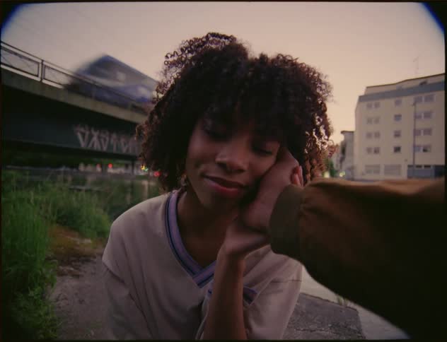 A woman is standing outside as a man has his hand on her face and a train passes on the trestle in the distance