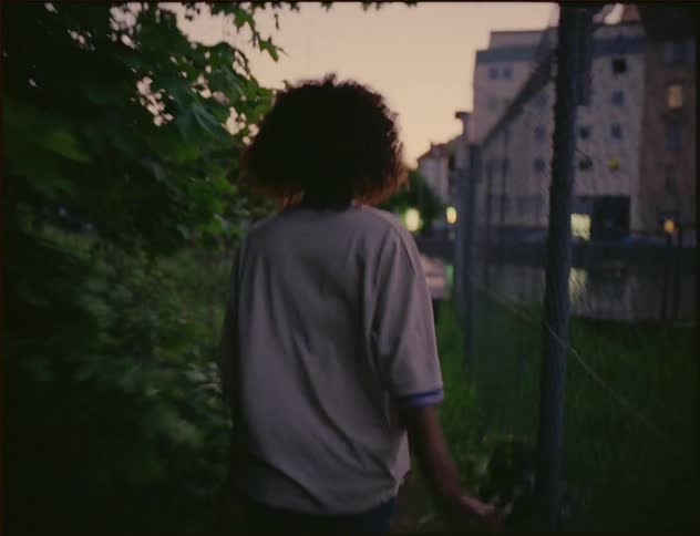 Young woman running along fence toward river in city motioning someone to follow her