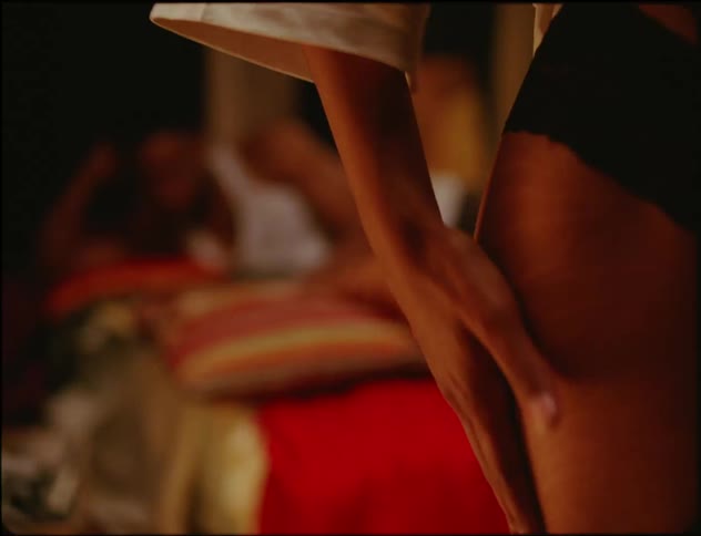 A woman stands up in her bedroom while her partner lies in bed