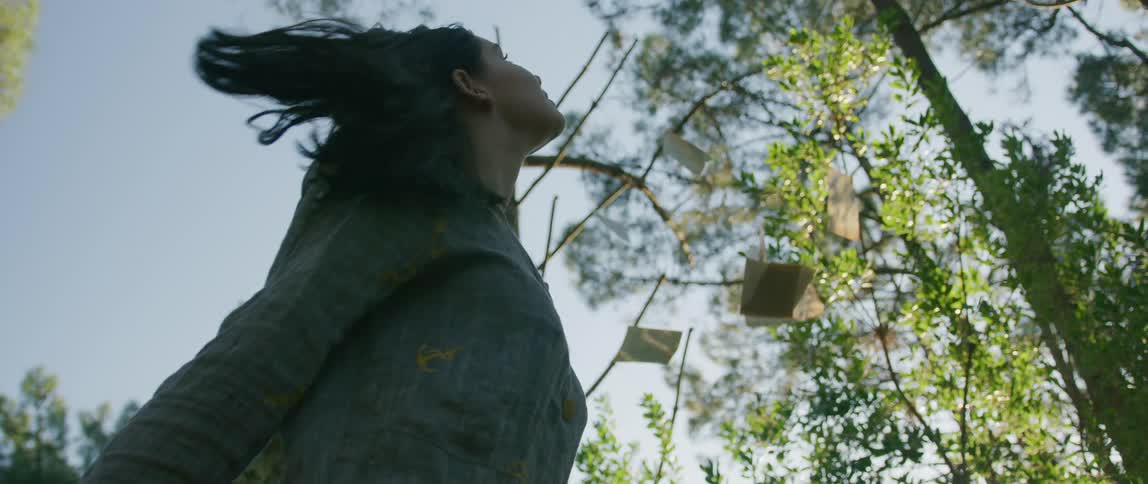 A girl tosses small squares of paper in the air as she twirls in a forest on a sunny day
