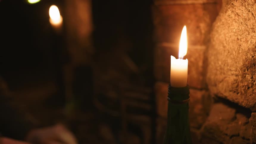 Candle flames illuminate a room as they glow in the darkness and a person is sitting nearby
