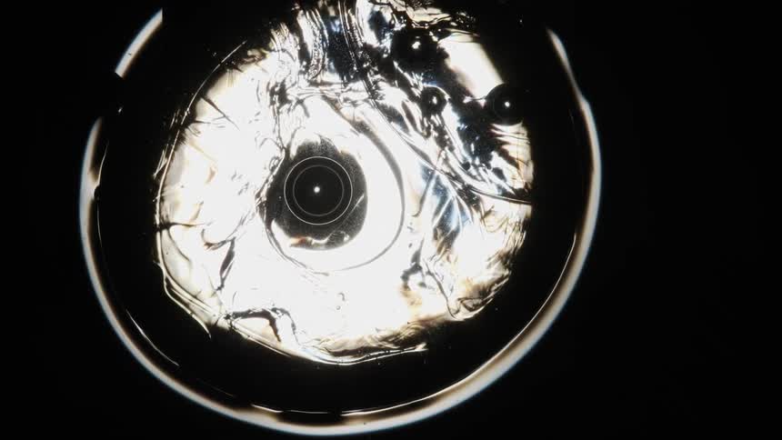Dark orbs move inside a sphere reflecting light as it ripples and moves in a black area