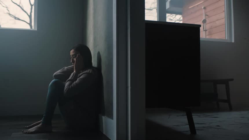 Young sad and depressed woman sits on the floor of a room near a window