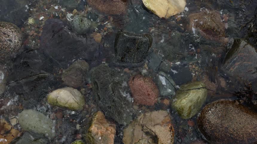 Waves roll over multicolored stones on beach