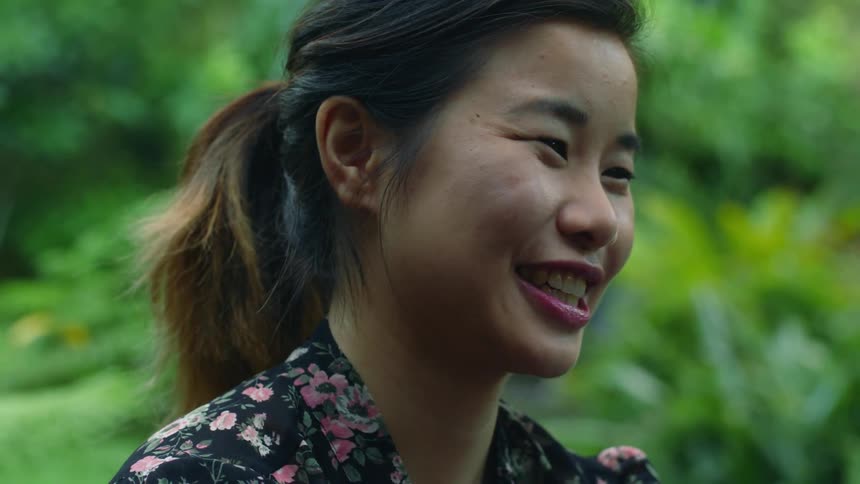 A teenage girl is smiling and laughing as she moves her hands and there are trees in the distance