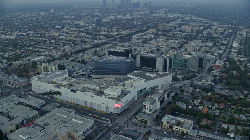 Aerial footage at sunrise of the Beverly Center and Cedars-Sinai Medical Center orbiting above Beverly Hills CA with cloudy skies and a medical and retail center in view