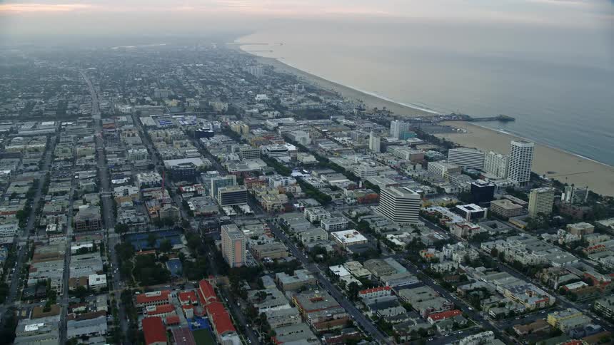 Fly over the residential and office areas near Santa Monica Pier during sunrise providing a wide angle view of the shoreline and beach on the west coast of Southern California