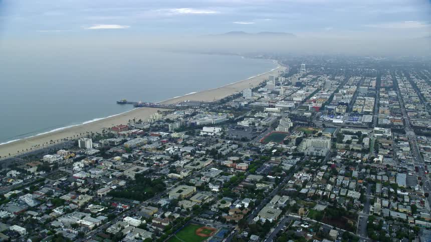 An epic shot of Santa Monica Pier approaching during sunrise flying over the residential and seaside neighborhoods in the westside of Los Angeles California