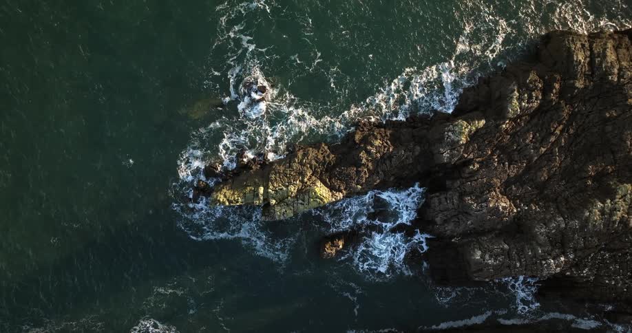 Birds eye view of ocean waves hitting shoreline around an island