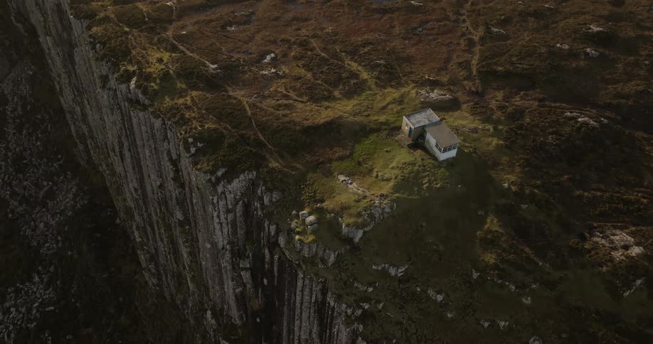 The flat roof of a home alone on the edge of sheer cliffs with a mountain lake behind
