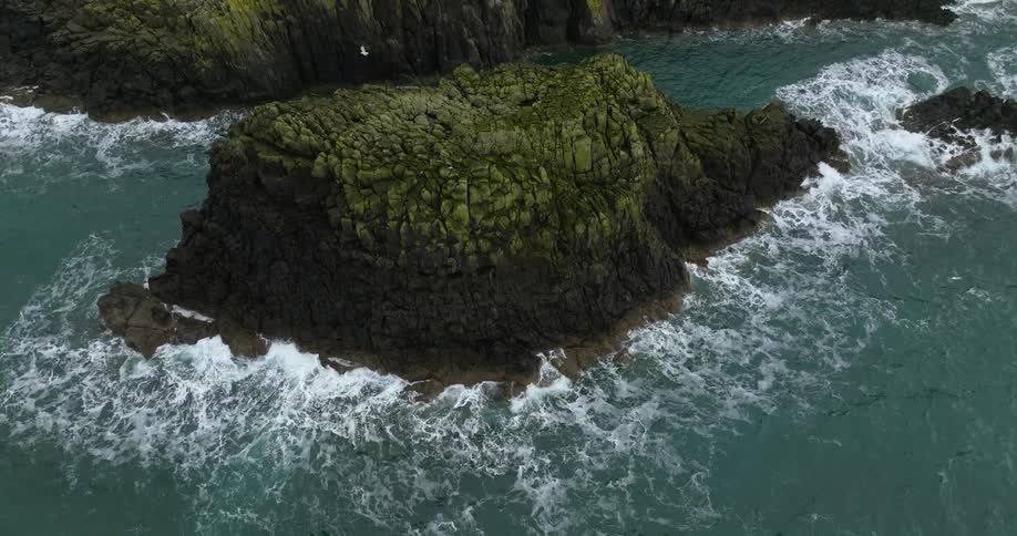 An aerial view of ocean waves crashing into a rocky island