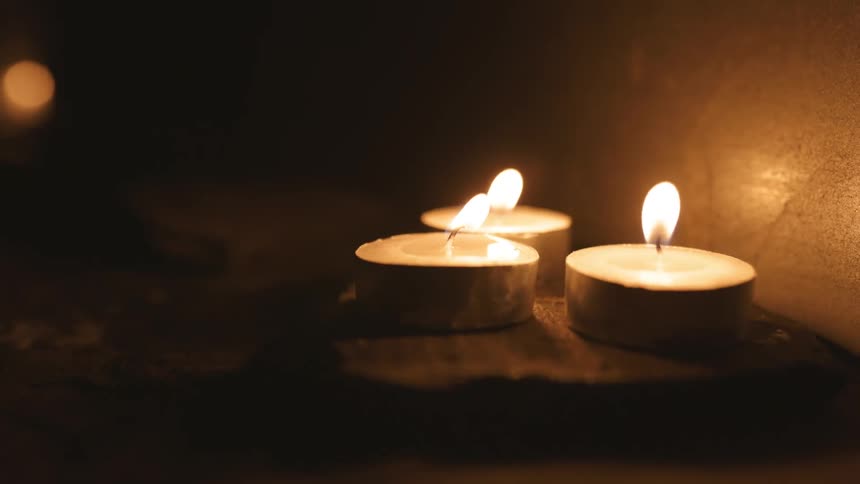 Flames flicker as three small candles sit on a table in the darkness