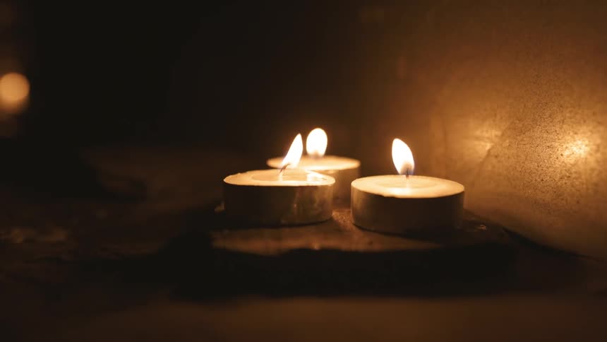 Flames flicker and are blown out as three small candles sit on a table in the darkness