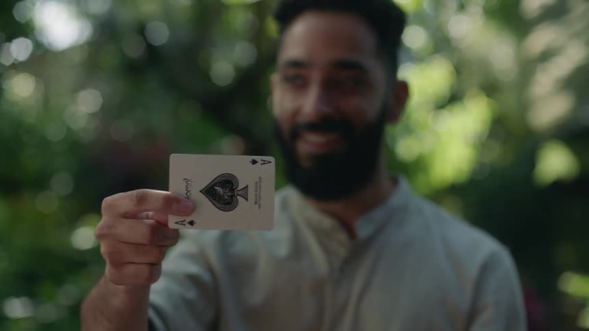 Man sitting outdoors turns king of hearts into an ace during a magic trick