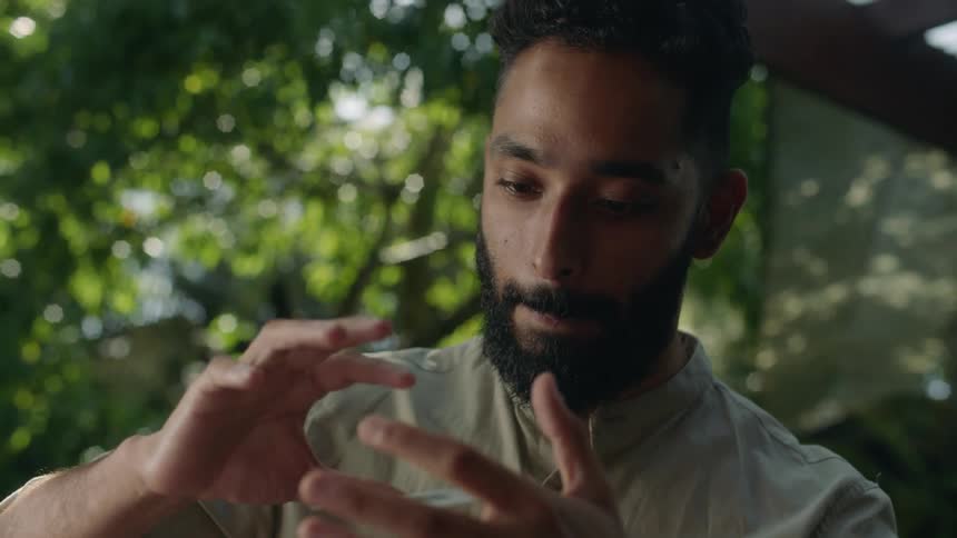 A man levitates a playing card in between his hands floating it up and down before blowing it away