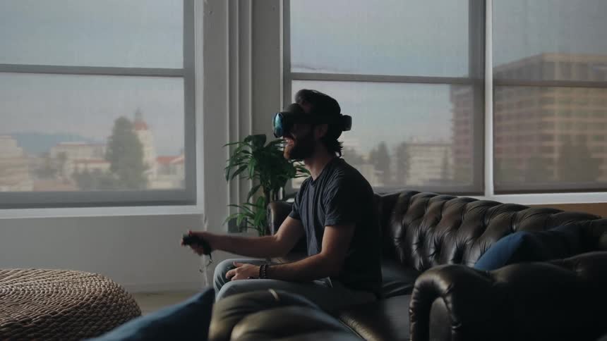 A man plays a virtual reality game while sitting on the couch