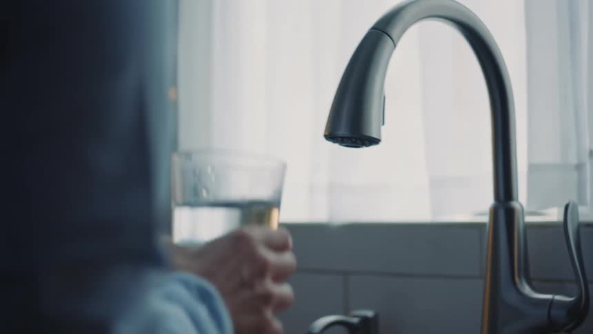 A person fills a glass of water and drinks