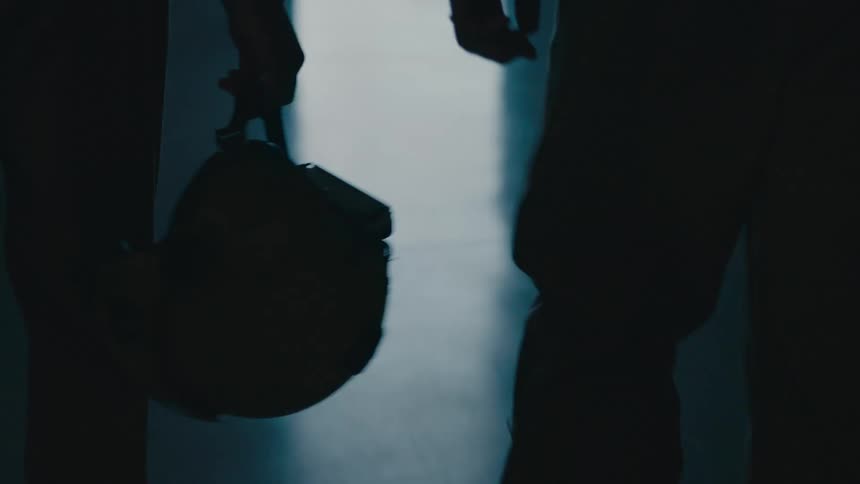 Silhouette of a couple of pilots walking inside a dark hangar towards a helicopter outside