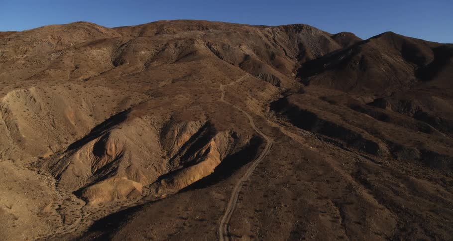 An aerial of a desert mountain with canyons and a road traveling throughout