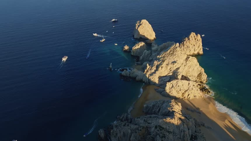 Boats speed past a beach connected to sea stacks in the ocean