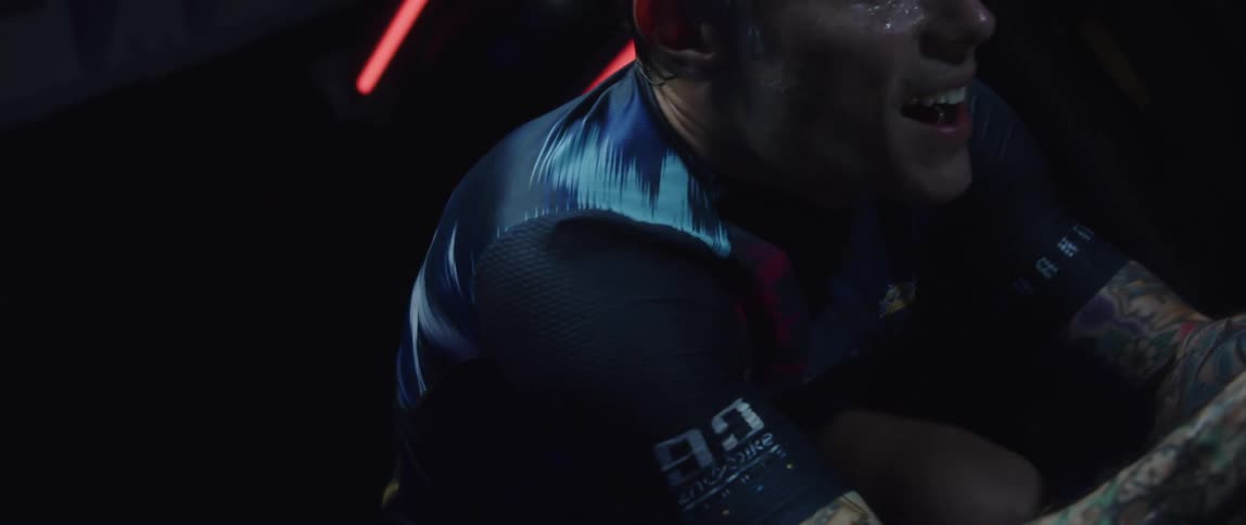 A sweating man pedals hard on an exercise bike in a dark room