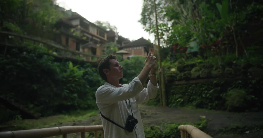 Man stands on bamboo bridge taking pictures with apartment buildings in the background