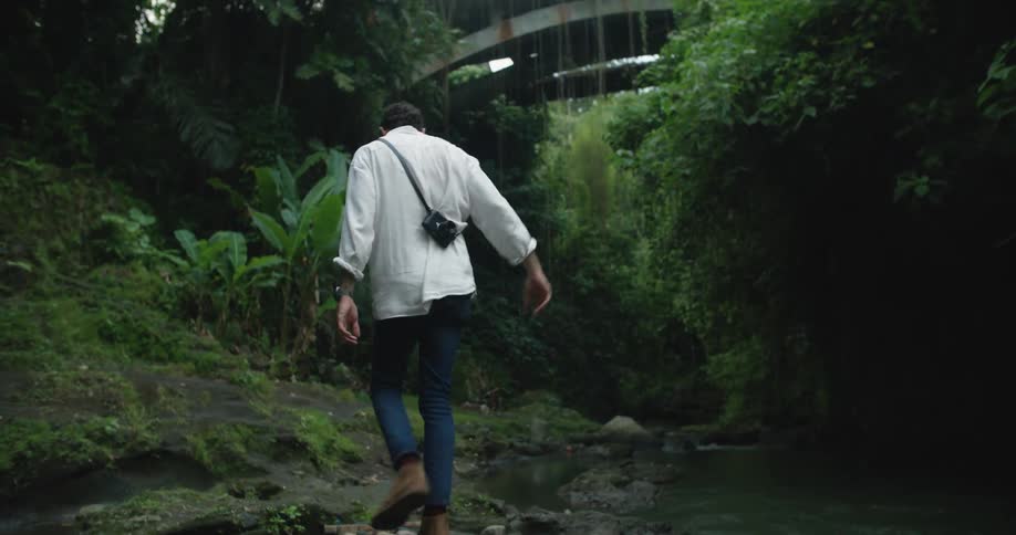 Man carrying a camera crosses over a makeshift bridge over a small stream