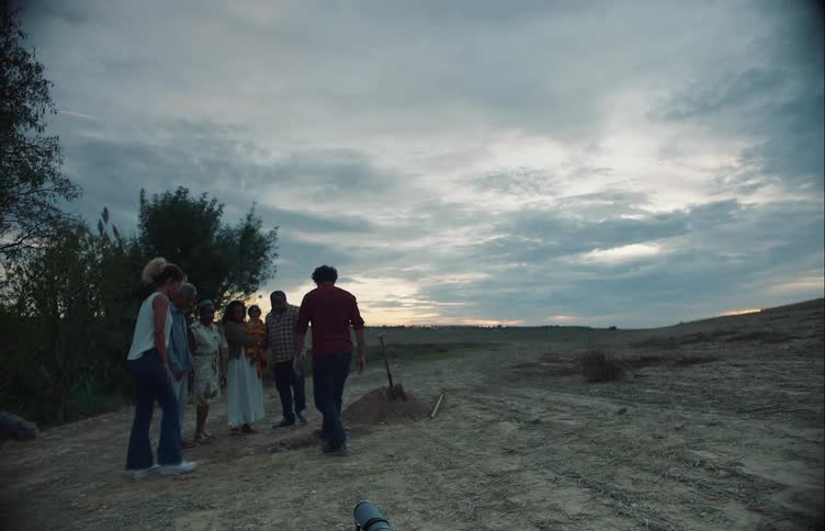 Family gathers around the grave of a pet in the countryside at evening