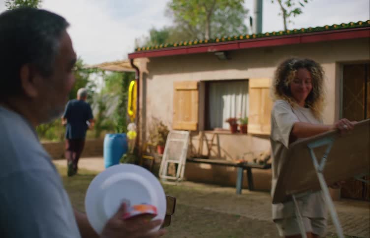 A man is drying a plate for a party as a woman carries a table outside