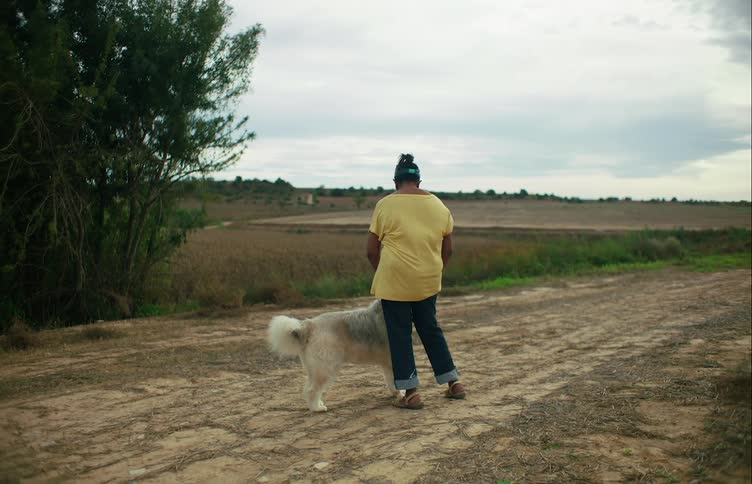 Wind is blowing a womans shirt when a dog walks up and she pets his head