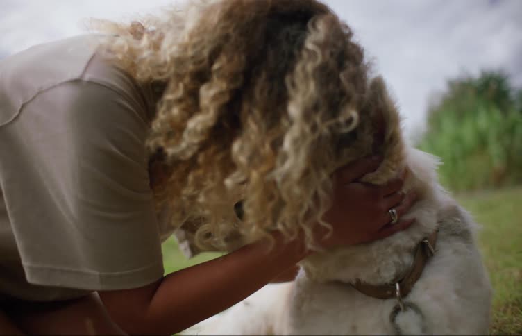 Woman kneels on the ground petting and cuddling chained dog