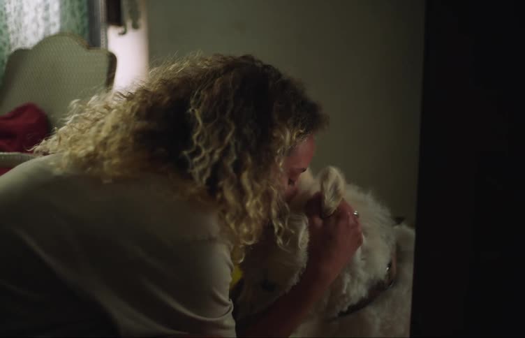 A young woman pets and kisses a dog before walking out of frame