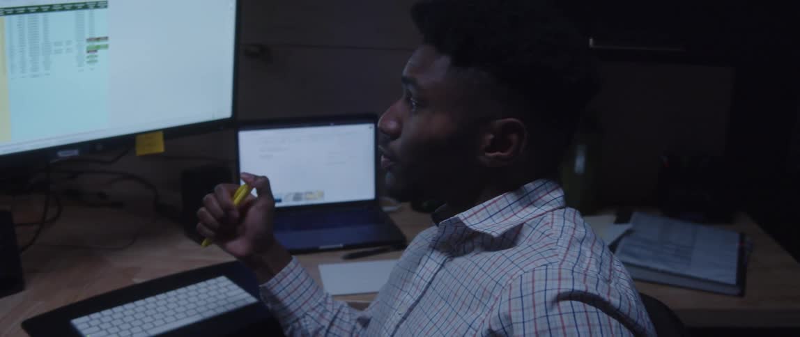 A man sitting at his work desk clicking a highlighter in his hand while he turns and talks to someone