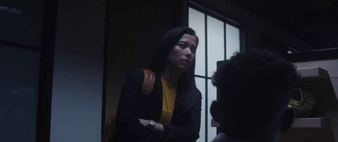 A man is sitting at a desk talking to a woman standing next to him with a bag over her shoulder